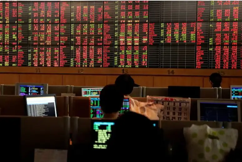Traders are seen in front of a screen with trading figures in red at Thailand Stock Exchange
